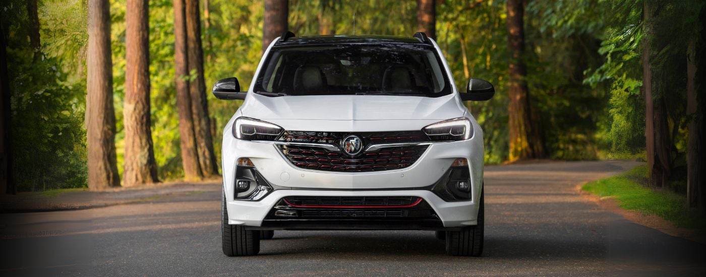 Head-on view of a white 2020 Buick Encore GX ST driving a tree-lined road.
