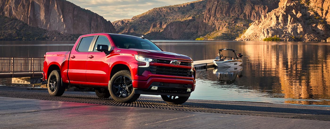 Red 2022 Chevy Silverado 1500 Z71 parked near a lake with a boat in the water.