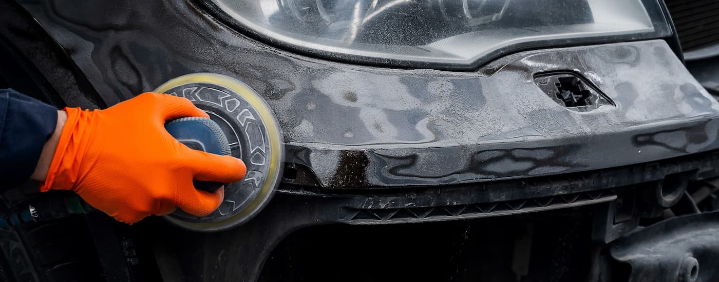 Person using a buffer on the bumper on a black car