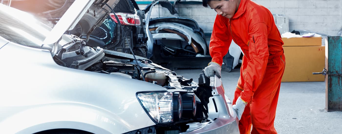 A technician working under the hood of a silver vehicle.