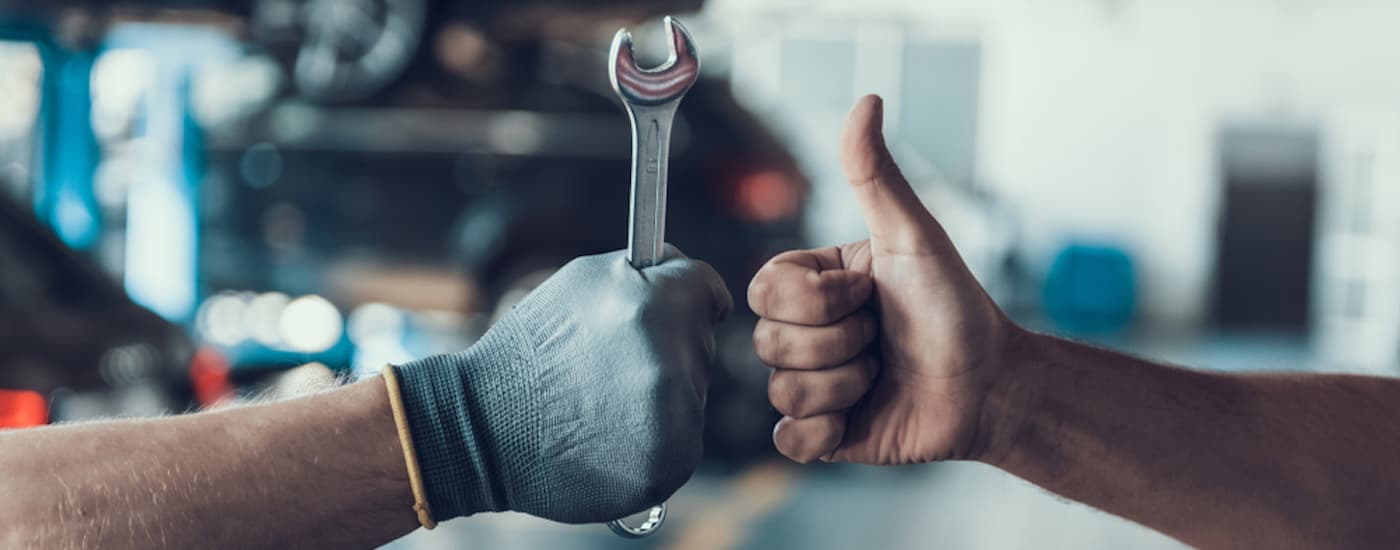 Gloved hand holding a wrench next to a hand with a thumbs up.