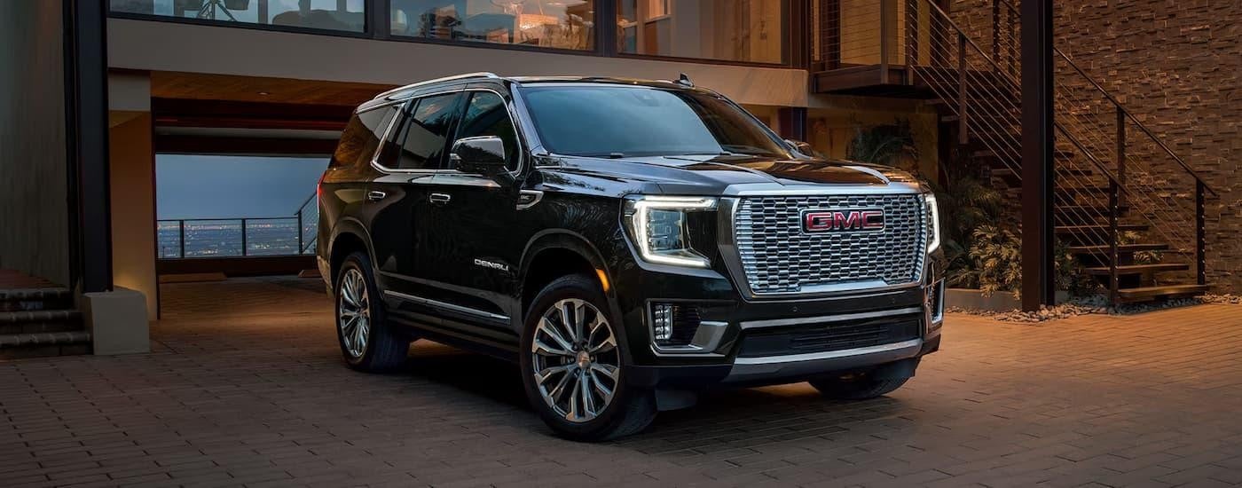 Black 2024 GMC Yukon parked in a driveway near a used car dealership