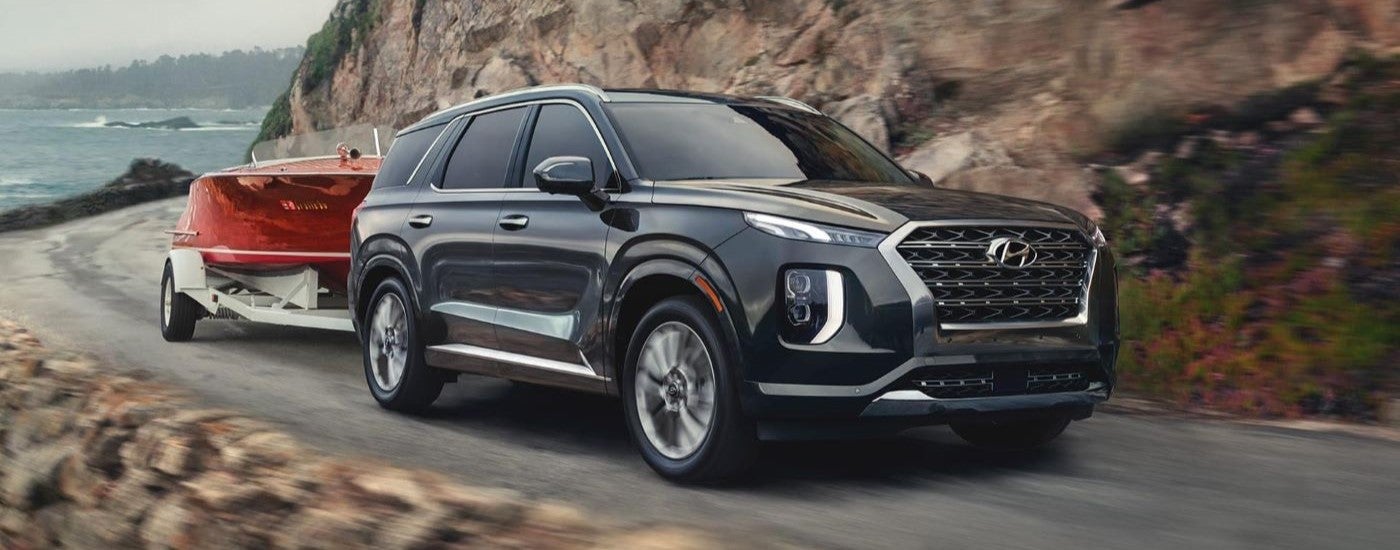 Black 2020 Hyundai Palisade towing a boat around a bend after visiting a used car dealership near Detroit.